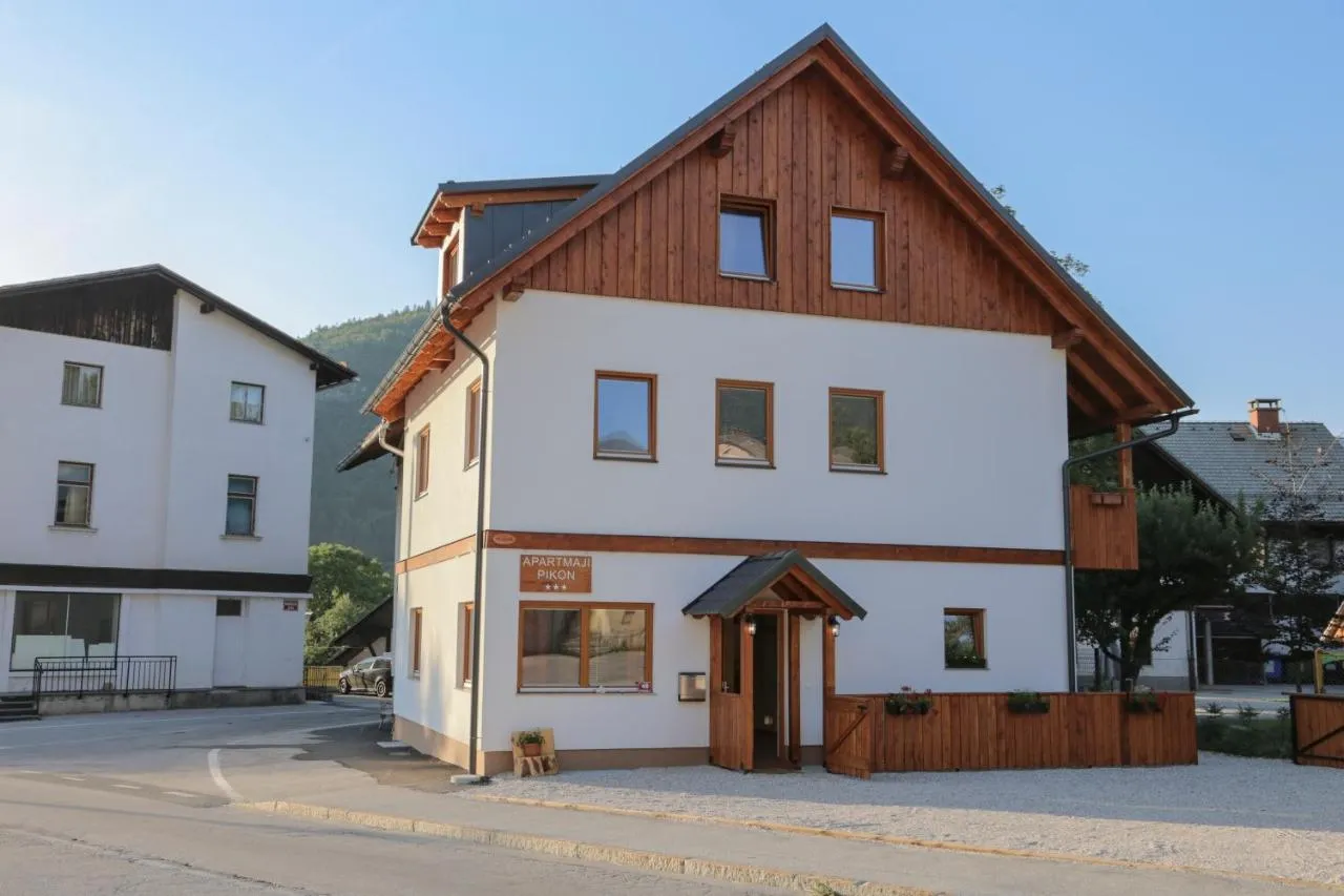 Bela hiša z lesenim čelom in napisom Apartmaji Pikon ob Triglavski cesti
